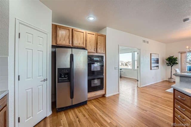 kitchen featuring black double oven, a notable chandelier, light hardwood / wood-style floors, stainless steel fridge with ice dispenser, and a textured ceiling