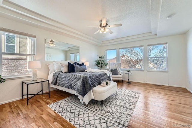 bedroom with a raised ceiling, a textured ceiling, ceiling fan, and light hardwood / wood-style floors