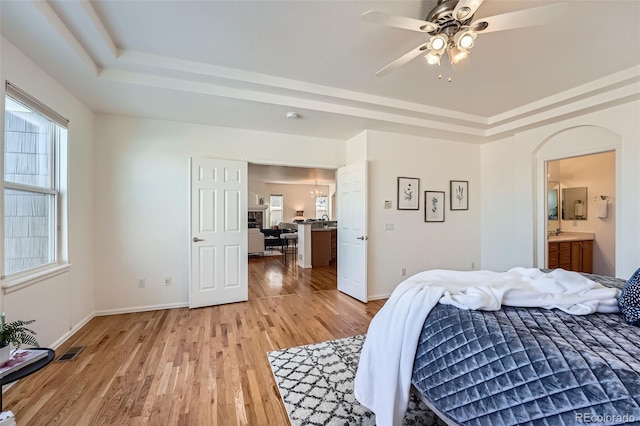 bedroom featuring a raised ceiling, light wood-type flooring, connected bathroom, and ceiling fan