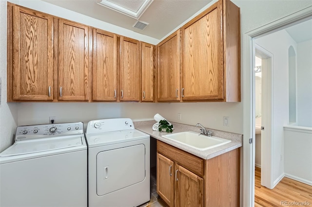 laundry area featuring cabinets, separate washer and dryer, sink, and light wood-type flooring