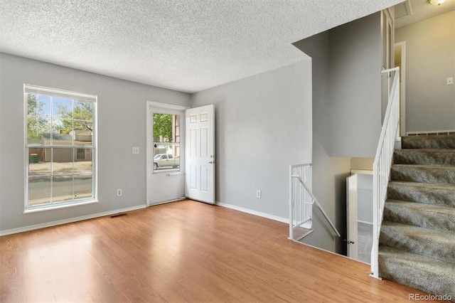 foyer entrance featuring healthy amount of natural light, wood finished floors, a textured ceiling, and baseboards