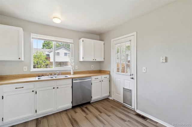 kitchen featuring stainless steel dishwasher, a sink, white cabinets, and healthy amount of natural light