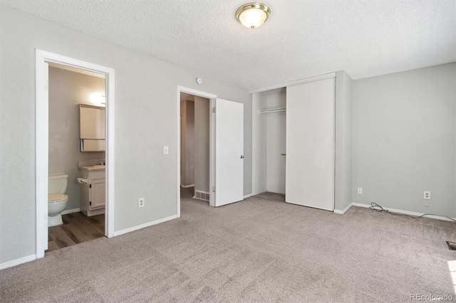 unfurnished bedroom with carpet flooring, a closet, a textured ceiling, ensuite bath, and baseboards