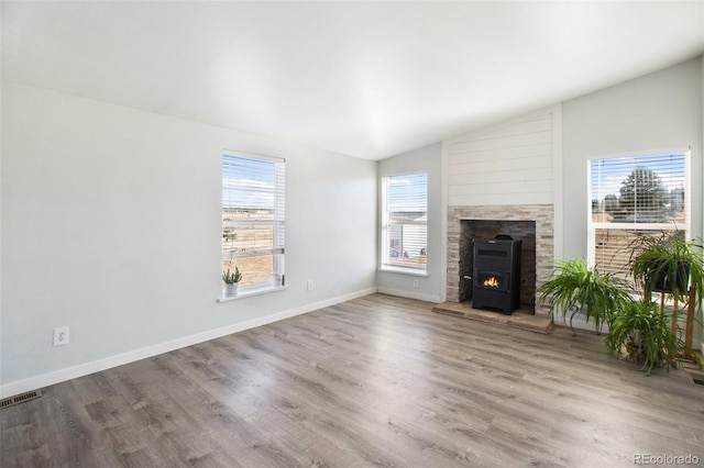 unfurnished living room featuring a wood stove, a healthy amount of sunlight, vaulted ceiling, and wood-type flooring