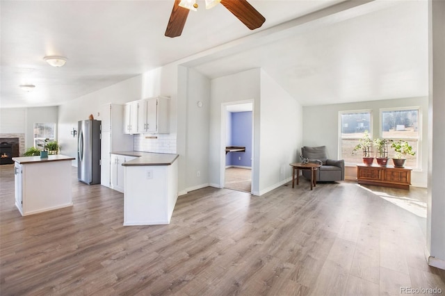 kitchen with stainless steel fridge, light wood-type flooring, tasteful backsplash, white cabinetry, and lofted ceiling