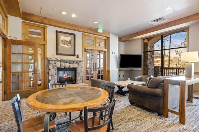 living room featuring french doors, plenty of natural light, a stone fireplace, and beamed ceiling