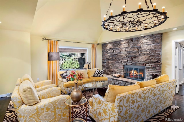 living room with a high ceiling, a stone fireplace, hardwood / wood-style floors, and an inviting chandelier