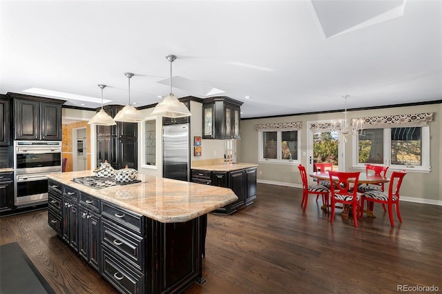 kitchen with appliances with stainless steel finishes, hanging light fixtures, dark hardwood / wood-style floors, a kitchen island, and a chandelier