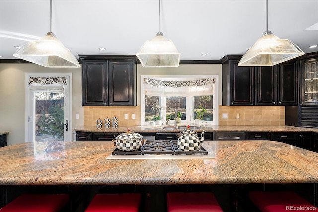 kitchen with a breakfast bar area, hanging light fixtures, a kitchen island, stainless steel gas stovetop, and decorative backsplash