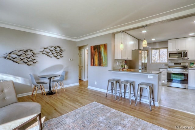 kitchen with pendant lighting, white cabinets, stainless steel appliances, and light hardwood / wood-style floors