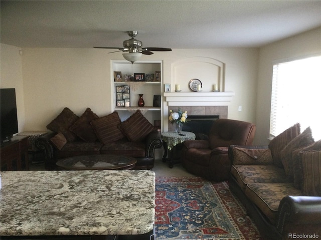 carpeted living room with a textured ceiling, a tiled fireplace, and ceiling fan