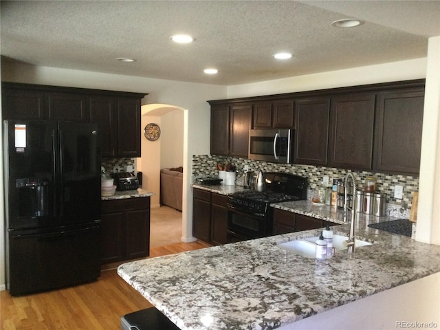 13674 Plaster Cir, Broomfield, CO 80023 - kitchen featuring black appliances, arched walkways, a sink, light stone counters, and dark brown cabinetry