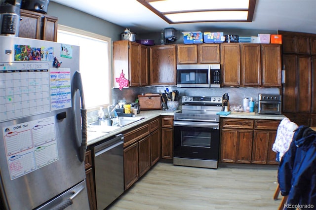 kitchen featuring light wood finished floors, light countertops, appliances with stainless steel finishes, and a sink