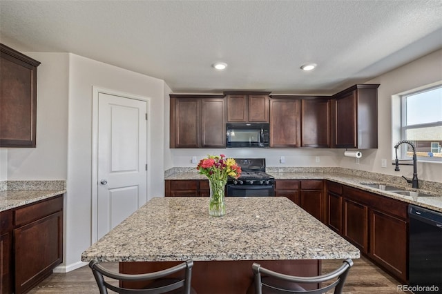 kitchen with a sink, dark wood-style flooring, a kitchen breakfast bar, and black appliances