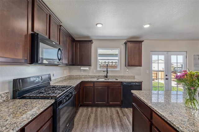kitchen featuring french doors, light stone counters, light wood finished floors, a sink, and black appliances