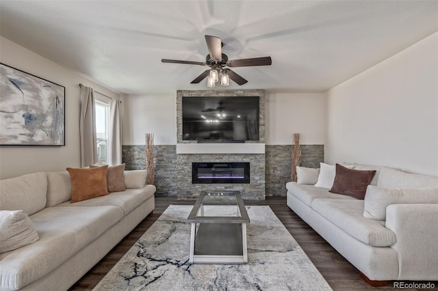living room with a stone fireplace, ceiling fan, and dark wood-style floors
