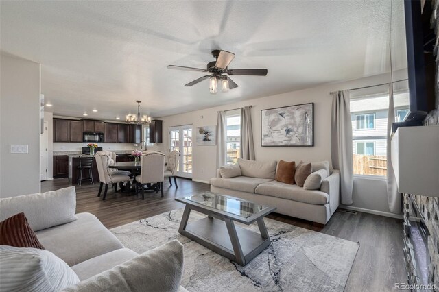 living room with baseboards, dark wood-style flooring, a healthy amount of sunlight, and ceiling fan with notable chandelier
