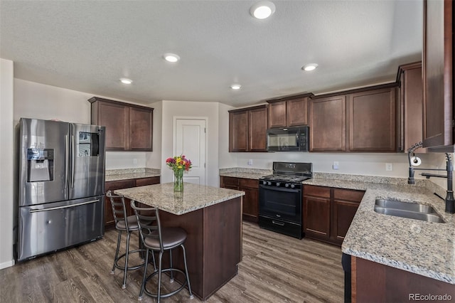 kitchen with dark wood-style flooring, dark brown cabinetry, a sink, a kitchen island, and black appliances