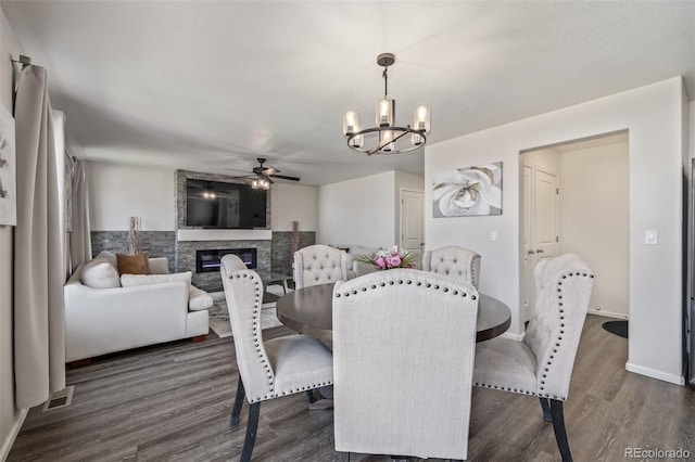 dining space with baseboards, a stone fireplace, dark wood finished floors, visible vents, and ceiling fan with notable chandelier