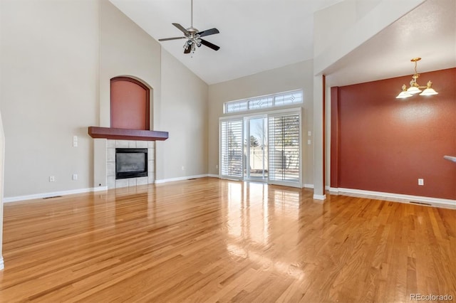 unfurnished living room featuring ceiling fan with notable chandelier, light wood-type flooring, high vaulted ceiling, and a fireplace