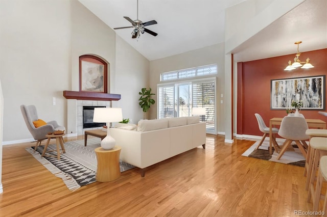 living room featuring a tile fireplace, ceiling fan with notable chandelier, light hardwood / wood-style floors, and high vaulted ceiling