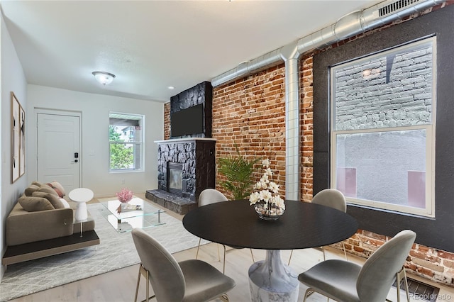 dining room featuring brick wall, a stone fireplace, and hardwood / wood-style floors