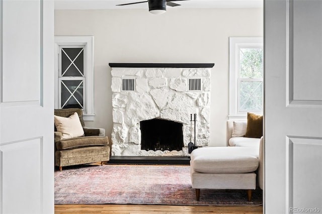 living room with a stone fireplace, ceiling fan, and hardwood / wood-style flooring