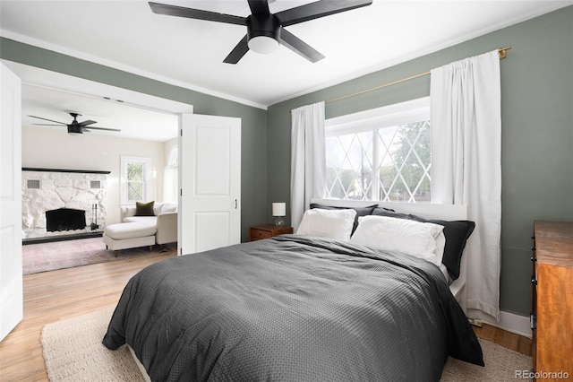 bedroom featuring ceiling fan, light hardwood / wood-style floors, a stone fireplace, and ornamental molding