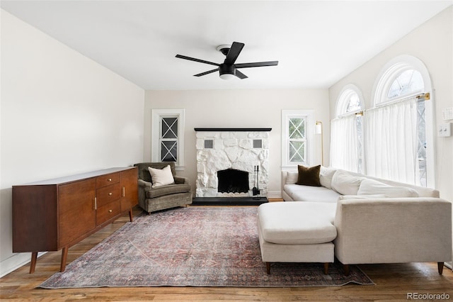 living room with a stone fireplace, ceiling fan, and hardwood / wood-style floors