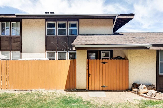 exterior space featuring fence, a gate, stucco siding, and roof with shingles