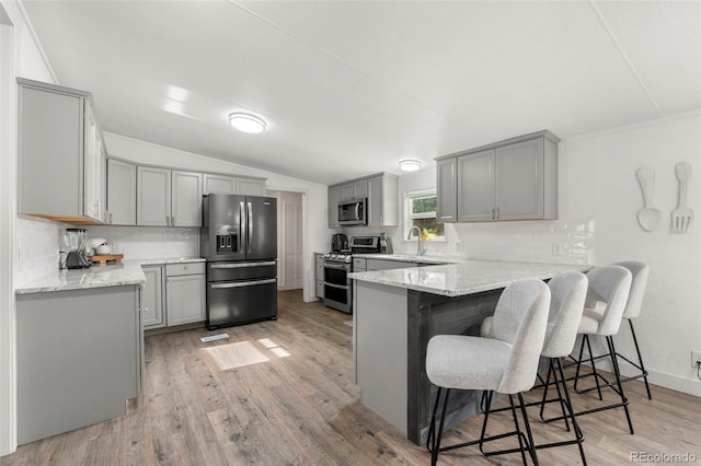 811 Plum Ave N, Lochbuie, CO 80603 - kitchen with stainless steel appliances, gray cabinetry, a peninsula, backsplash, and light wood-style floors