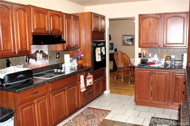 kitchen featuring ventilation hood, backsplash, light tile flooring, black appliances, and dark stone countertops