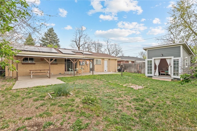back of house with fence, roof mounted solar panels, an outbuilding, a lawn, and a patio