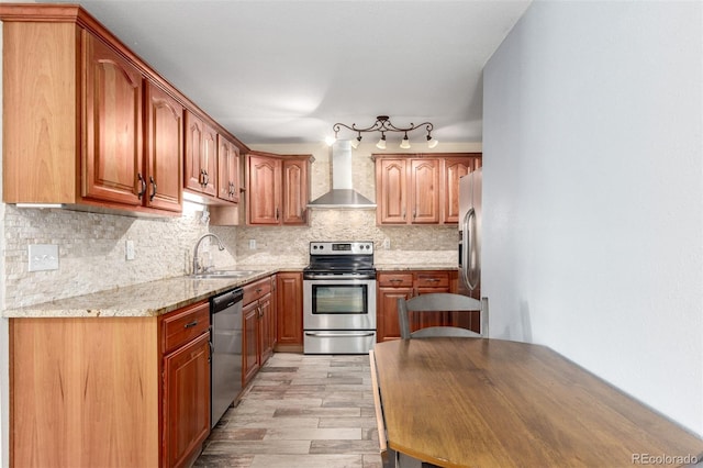 kitchen featuring tasteful backsplash, wall chimney range hood, light wood-type flooring, appliances with stainless steel finishes, and a sink