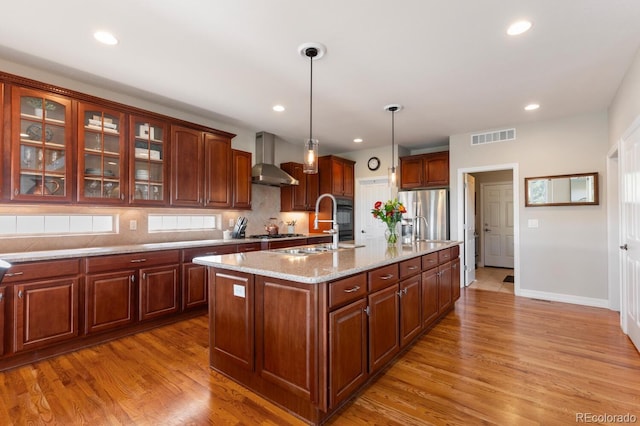 1519 Stonehill Ct, Castle Rock, CO 80104 - kitchen featuring wall chimney exhaust hood, appliances with stainless steel finishes, backsplash, a kitchen island with sink, and light wood finished floors