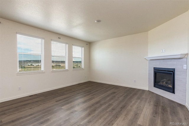 unfurnished living room with a tiled fireplace, a textured ceiling, and dark hardwood / wood-style flooring