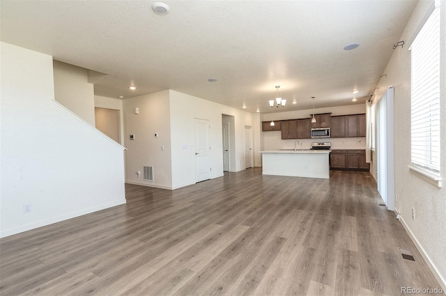 unfurnished living room with an inviting chandelier, a textured ceiling, hardwood / wood-style flooring, and sink