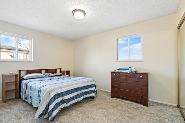 bedroom with light colored carpet, baseboards, and a textured ceiling