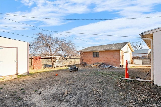 view of yard featuring a detached garage, an outbuilding, an outdoor fire pit, and fence