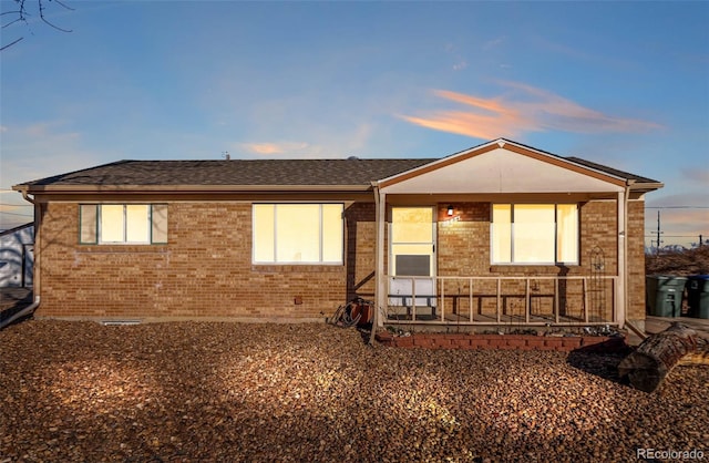 ranch-style home featuring covered porch, brick siding, and roof with shingles