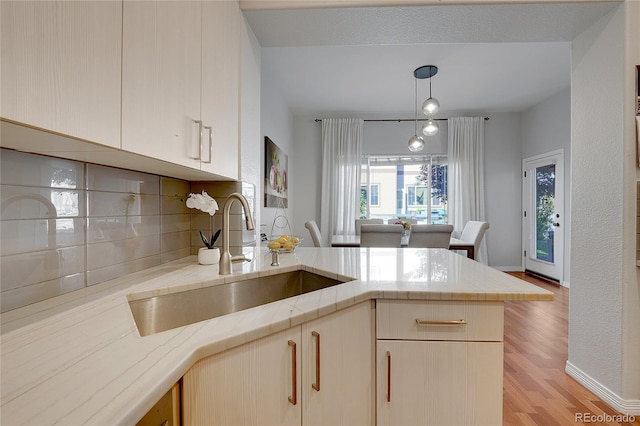 kitchen with decorative backsplash, hanging light fixtures, a peninsula, light countertops, and a sink