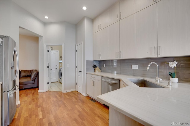 kitchen featuring backsplash, stainless steel appliances, sink, washer / dryer, and light hardwood / wood-style floors