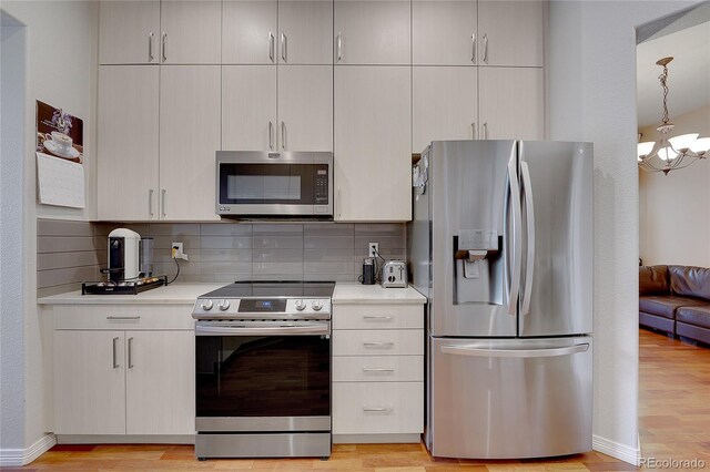 kitchen featuring tasteful backsplash, a notable chandelier, decorative light fixtures, appliances with stainless steel finishes, and light wood-type flooring