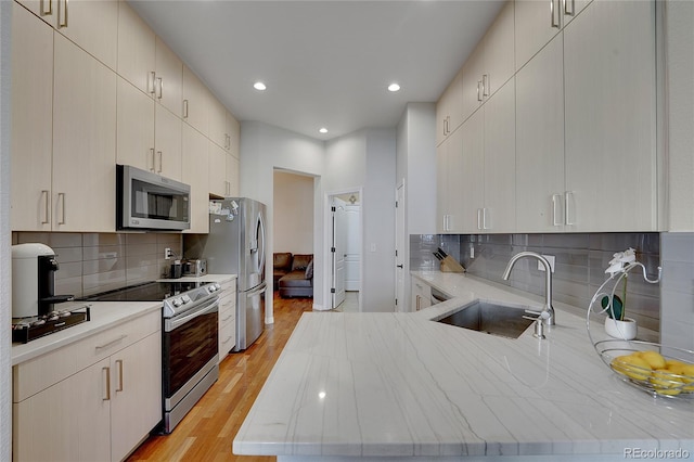 kitchen featuring sink, stainless steel appliances, tasteful backsplash, cream cabinets, and light wood-type flooring