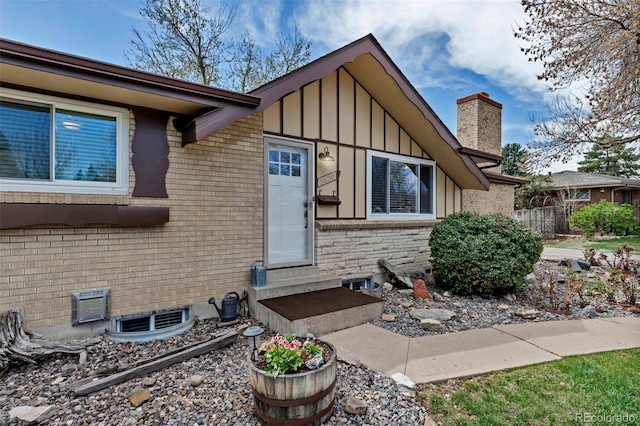 view of home's exterior with entry steps, board and batten siding, a chimney, fence, and brick siding