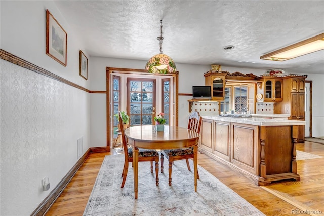 dining area featuring a textured ceiling, light wood-style floors, and baseboards