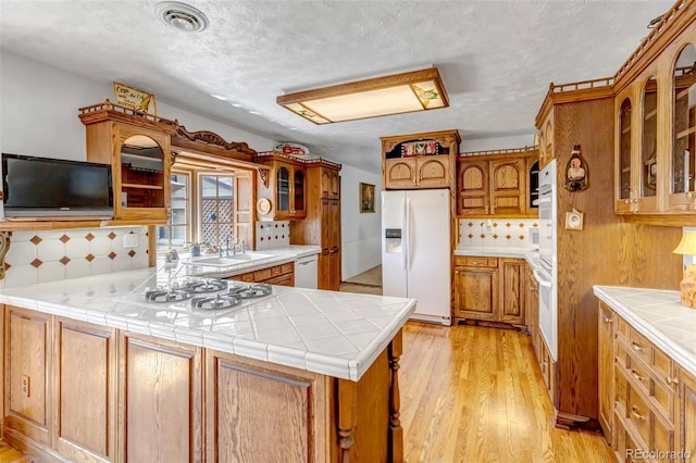 kitchen with white appliances, a sink, a peninsula, decorative backsplash, and light wood finished floors