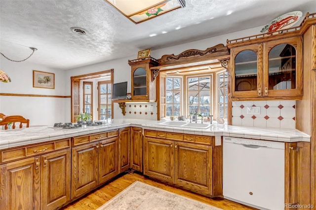 kitchen with white appliances, a sink, light wood finished floors, brown cabinets, and backsplash