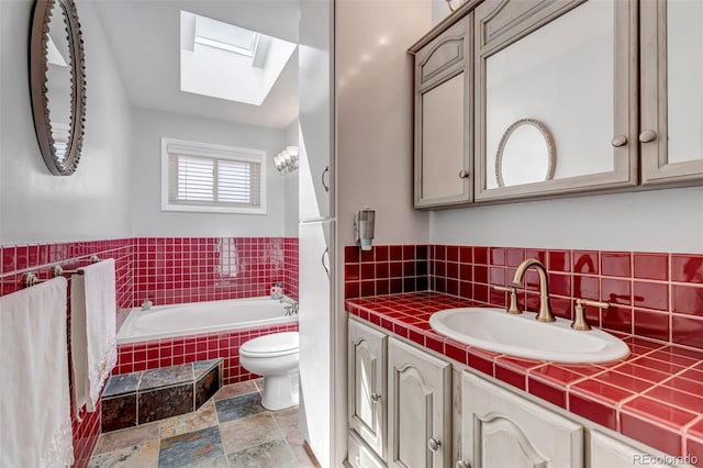 bathroom featuring a skylight, tiled tub, toilet, and vanity