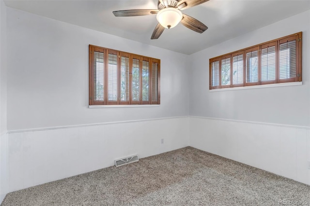carpeted empty room with ceiling fan and a wainscoted wall